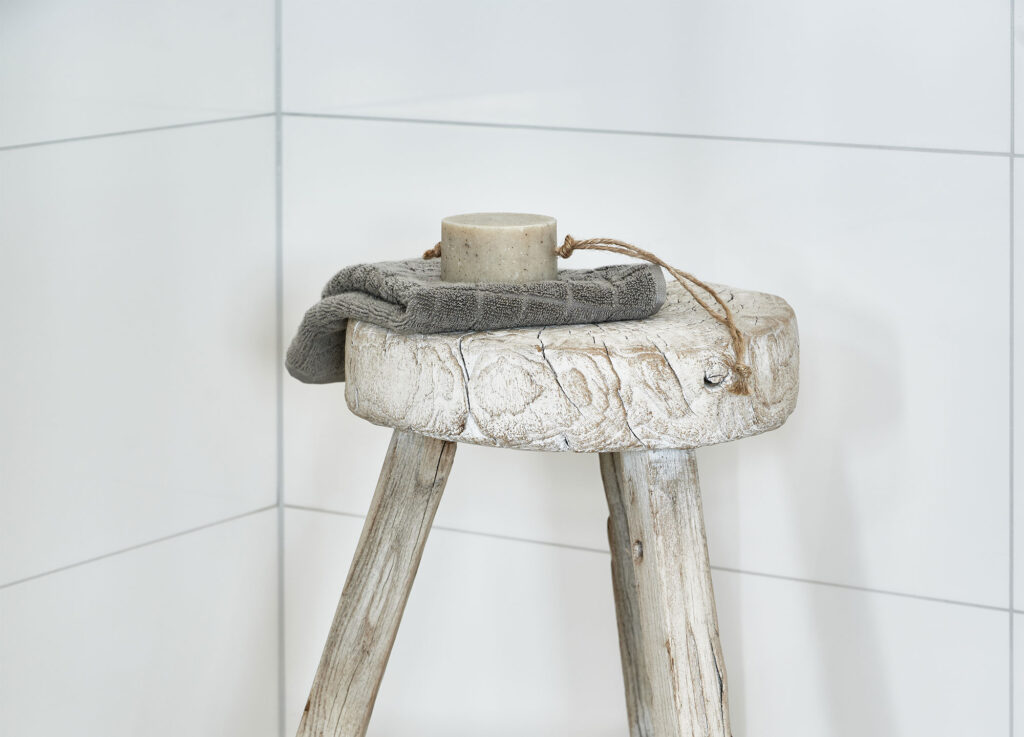 soap and grey towel on wooden stool in a bathroom with white tiles